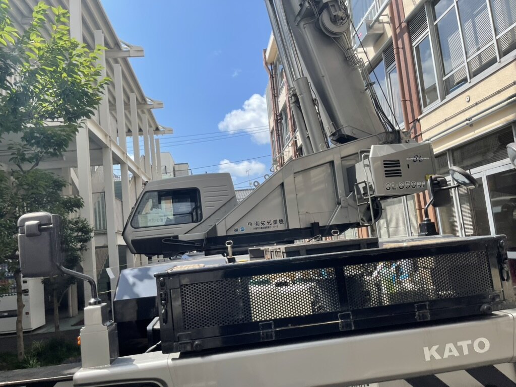 クレーンの荷台越しに見た、建物と街路樹の間の作業スペース